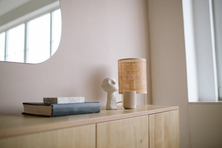 A minimalist wooden cabinet with books, a lamp, and artistic decor.
